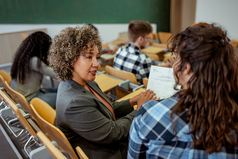 Portrait of Female University Tutor Talking With Female Student in Classroom at College Education Training Class